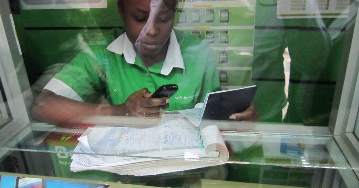 Safaricom attendant using a phone and tablet at an M-PESA counter